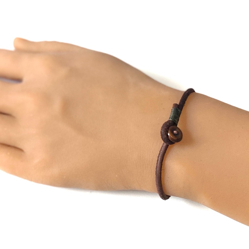 May include: A brown leather bracelet with a small, round, copper-colored button.