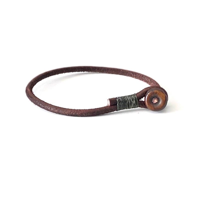May include: A brown leather bracelet with a wooden button closure. The button is a dark brown color with a lighter brown center.