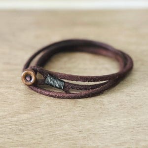 Puede incluir: Un brazalete de cuero marrón con cierre de botón de madera.