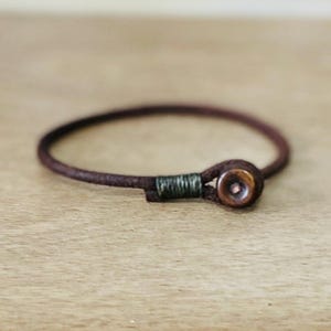 May include: A brown leather bracelet with a dark brown wooden bead and a green thread accent.