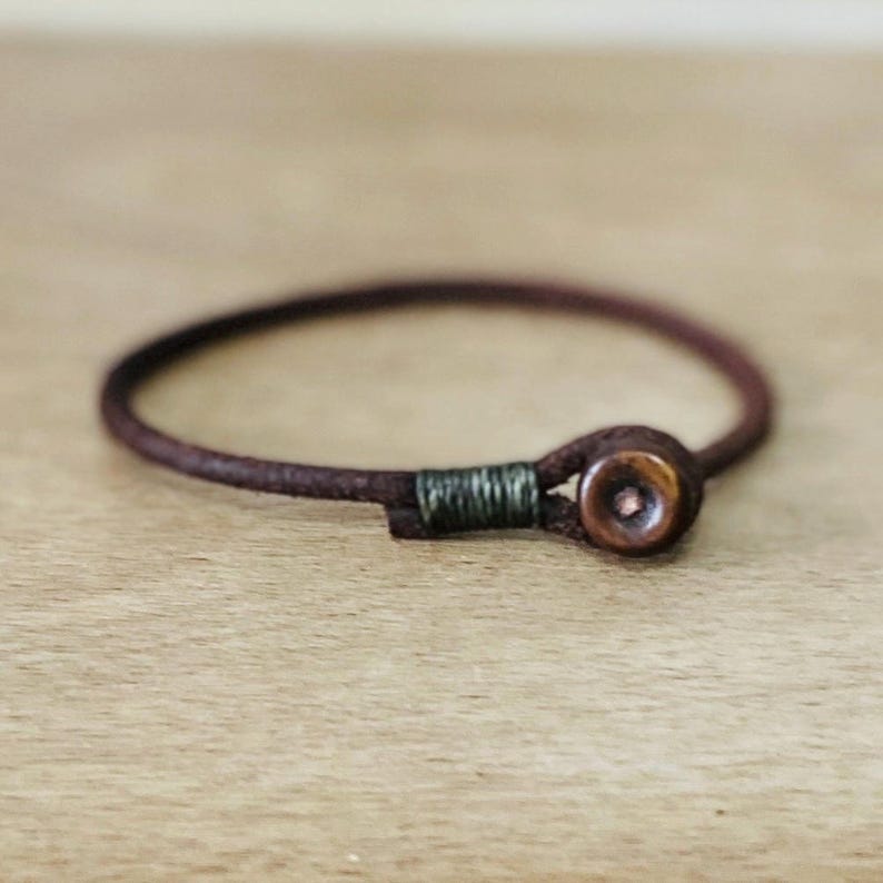 May include: A brown leather bracelet with a dark brown wooden bead and a green thread accent.