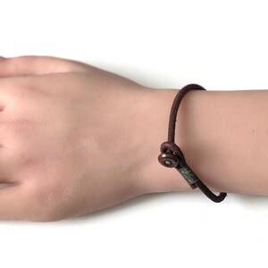 May include: A brown leather bracelet with a metal clasp. The bracelet is adjustable and has a simple design.