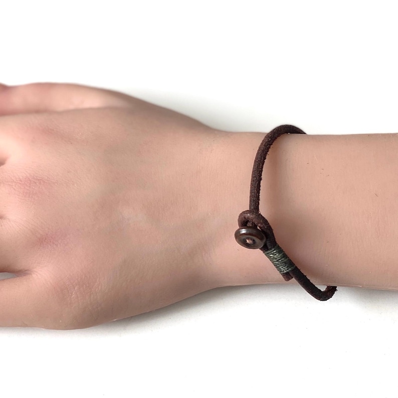 May include: A brown leather bracelet with a metal clasp. The bracelet is adjustable and has a simple design.