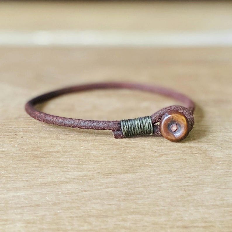May include: A brown leather bracelet with a small wooden bead and a green thread accent.