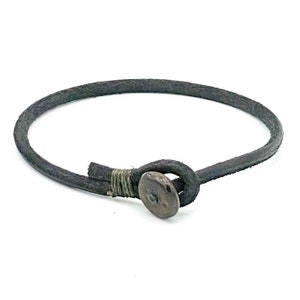 Puede incluir: Un brazalete de cuero negro simple con un cierre de botón de madera marrón.