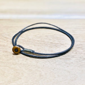 Könnte beinhalten: Ein schlichtes Armband aus schwarzem Lederband mit einem braunen Holzknopfverschluss.