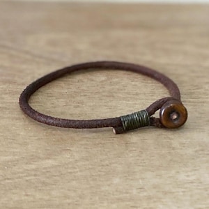 May include: A brown leather bracelet with a wooden button closure.