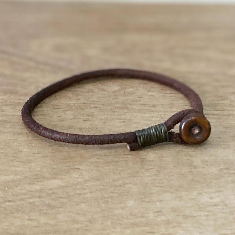 May include: A brown leather bracelet with a wooden button closure.