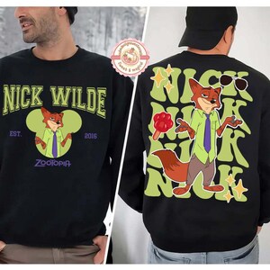 May include: Black sweatshirt featuring Nick Wilde from Zootopia. The front displays "Nick Wilde" in green lettering, with an image of Nick. The back has a larger Nick Wilde graphic with sunglasses and stars.