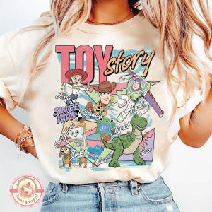 Pu&ograve; includere: Una t-shirt color crema con una stampa grafica colorata dei personaggi di Toy Story, tra cui Jessie, Woody, Buzz Lightyear, Rex e Slinky. Il design include il testo Toy Story, Since 1995 e i nomi dei vari personaggi raffigurati.