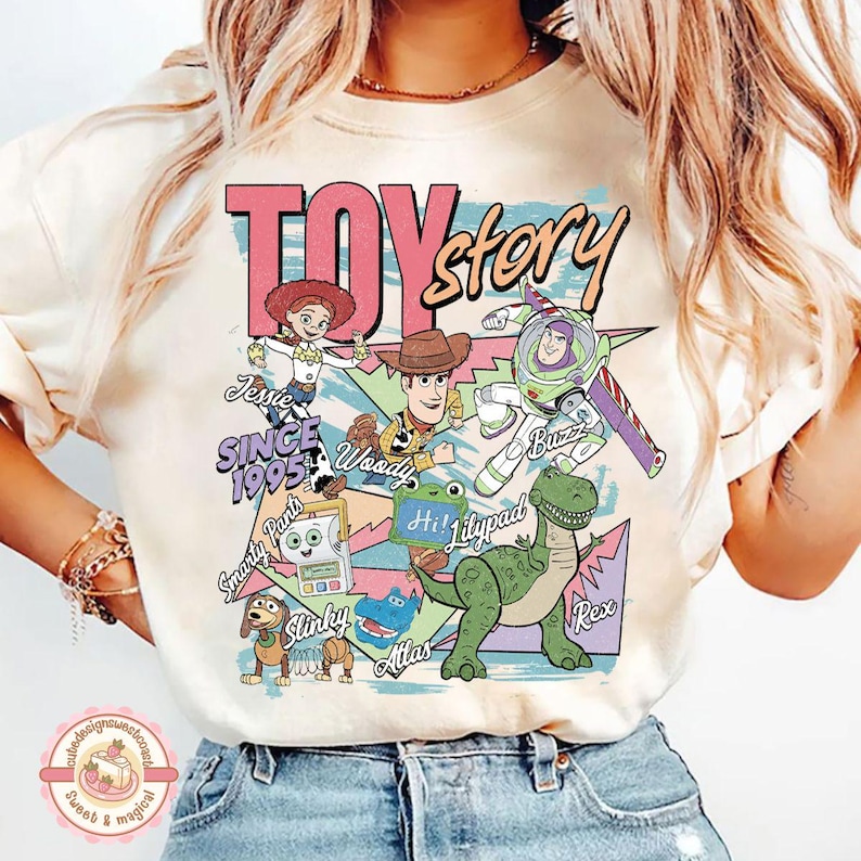 Pu&ograve; includere: Una t-shirt color crema con una stampa grafica colorata dei personaggi di Toy Story, tra cui Jessie, Woody, Buzz Lightyear, Rex e Slinky. Il design include il testo Toy Story, Since 1995 e i nomi dei vari personaggi raffigurati.