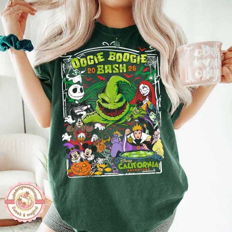 K&ouml;nnte beinhalten: Ein dunkelgr&uuml;nes Kurzarm-T-Shirt mit einem Grafikdruck und dem Text Oogie Boogie Bash 2026 California Adventure. Das Design zeigt verschiedene animierte Figuren, eine gro&szlig;e gr&uuml;ne Kreatur, einen K&uuml;rbis und einen Kessel in einem Rahmen.