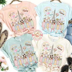 May include: Four pastel-colored t-shirts with a Disneyland theme. Each shirt features a graphic with the Eiffel Tower, Mickey Mouse, and other Disney characters. The word "Disneyland" is prominently displayed.
