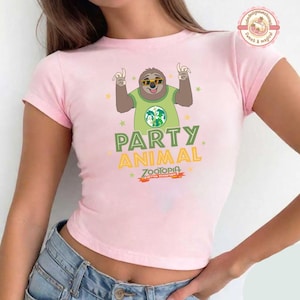 May include: A pale pink t-shirt with a cartoon sloth wearing sunglasses and a green shirt with a world map design. The text "PARTY ANIMAL" and "ZOOTOPIA" are printed on the shirt.