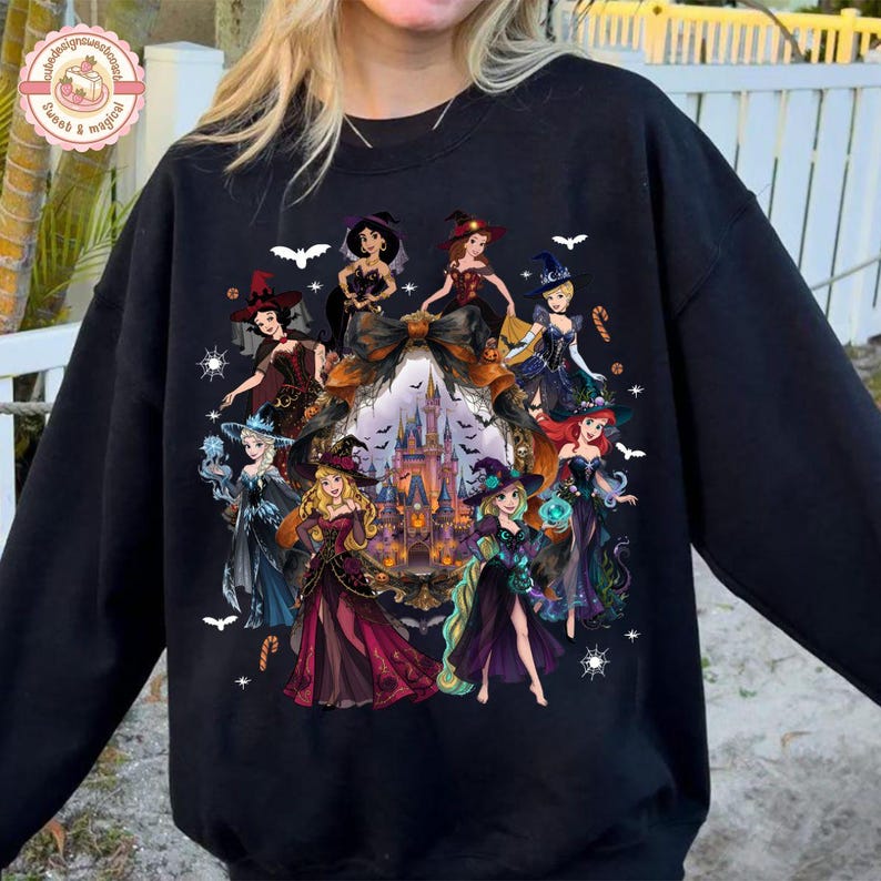 May include: A black crewneck sweatshirt featuring a graphic print of multiple animated female characters dressed in witch costumes. The design includes a central castle illustration surrounded by bats, spiderwebs, and candy canes in a dark color palette.