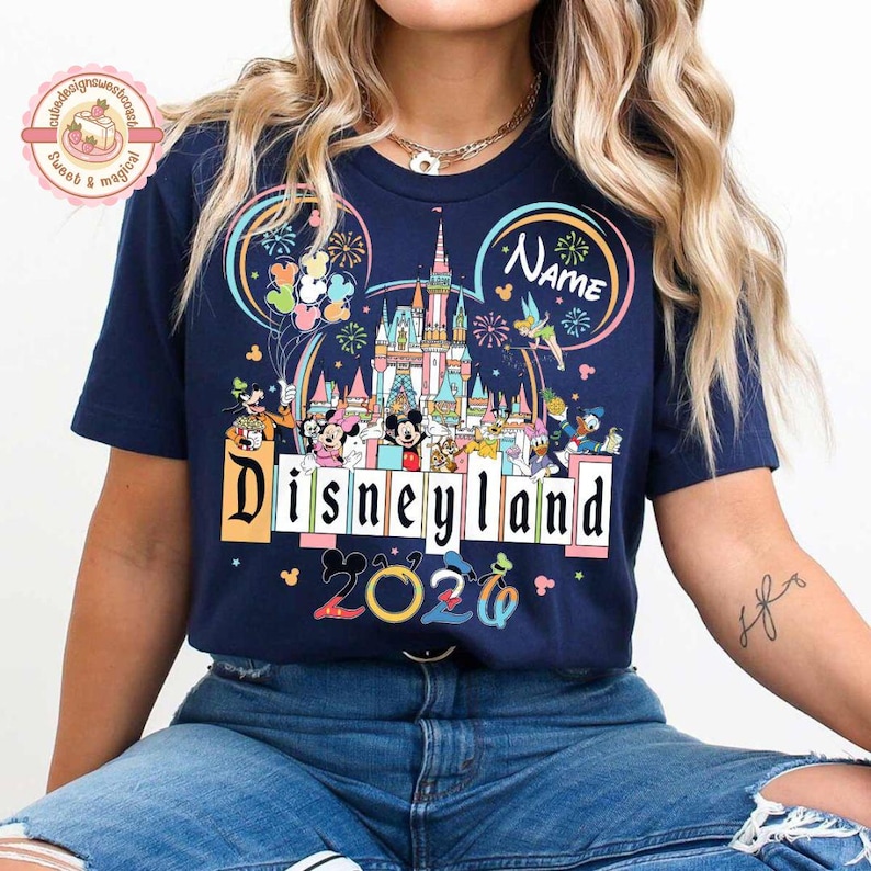 May include: Navy blue t-shirt featuring a colorful Disneyland graphic. The design includes the Disneyland castle, Mickey Mouse, and other characters. The text "Disneyland 2020" is also displayed.