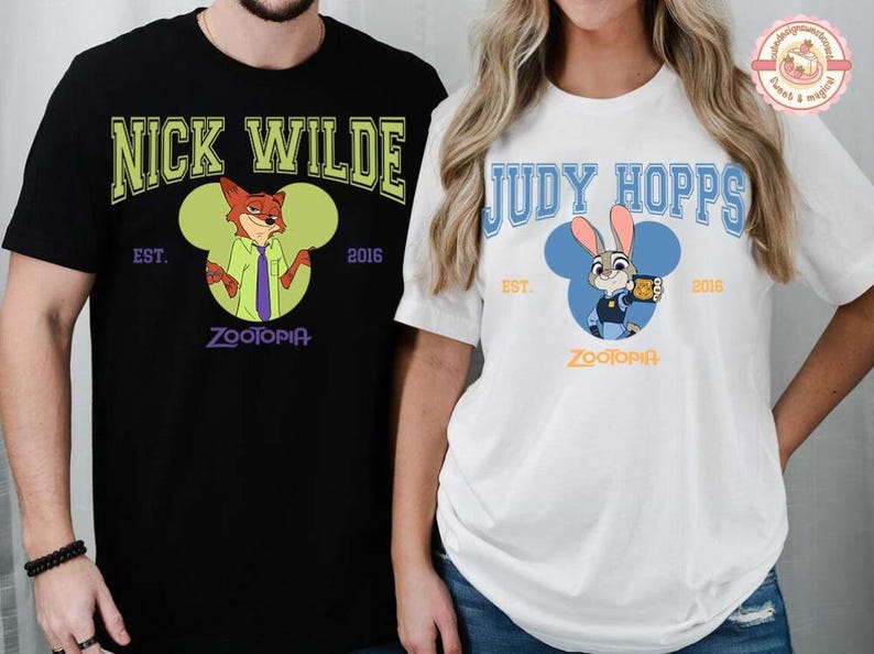May include: Black and white t-shirts featuring characters from the animated film Zootopia. One shirt displays "Nick Wilde" with a fox illustration, the other "Judy Hopps" with a bunny illustration. Both shirts have "Zootopia" text and the year "2016".
