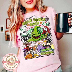 K&ouml;nnte beinhalten: Ein hellrosa T-Shirt mit einem Grafikdruck, der den Text "DOGIE BOOGIE 20 BASH 26" und "CALIFORNIA" enth&auml;lt. Das Design zeigt verschiedene Zeichentrickfiguren, eine gro&szlig;e gr&uuml;ne Kreatur, K&uuml;rbisse und Spinnennetze in einem rechteckigen Rahmen.