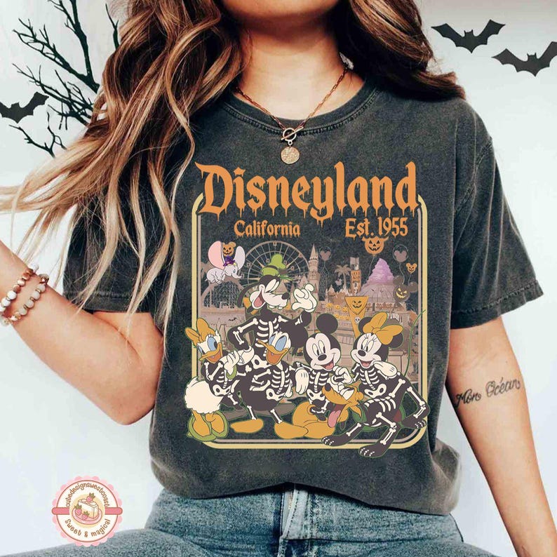 K&ouml;nnte beinhalten: Dunkelgraues T-Shirt mit einem Disneyland-Motiv und dem Text "Disneyland California Est. 1955". Das Design zeigt Disney-Figuren in Skelett-Kost&uuml;men mit Halloween-Thema. Das T-Shirt hat einen Vintage-Look.