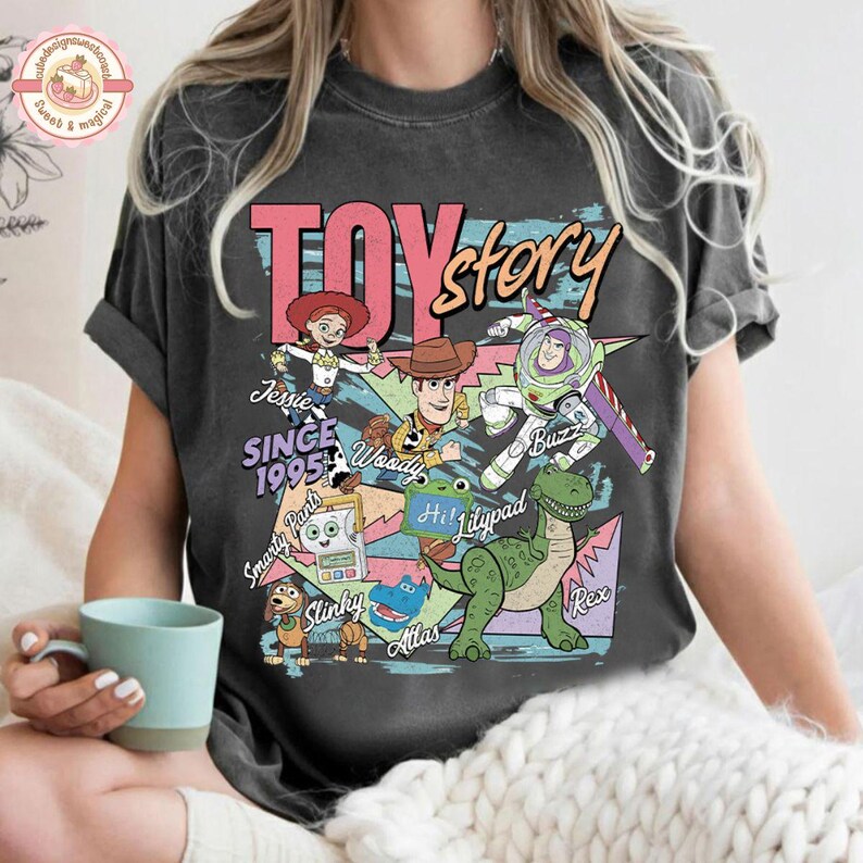Pu&ograve; includere: Una t-shirt a maniche corte grigio antracite con una stampa grafica colorata dei personaggi di Toy Story, tra cui Jessie, Woody, Buzz Lightyear, Slinky e Rex. Il testo riporta TOY story SINCE 1995, Smarty Pants, Hi! Lilypad e Atlas.