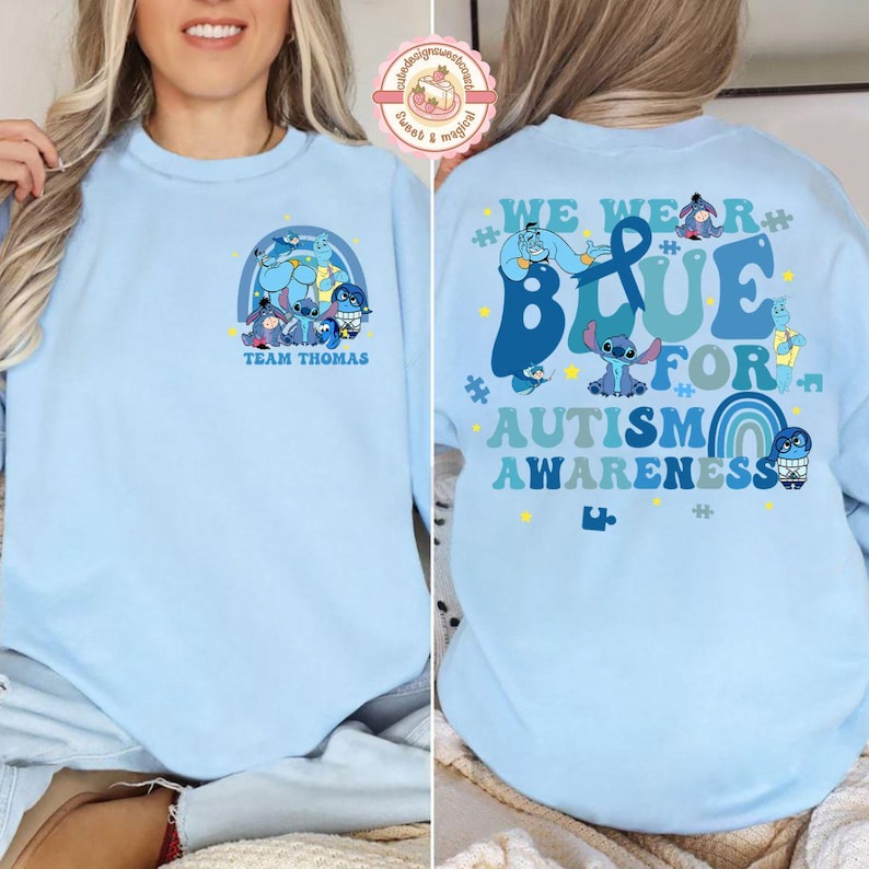 May include: Pale blue sweatshirt with a cartoon graphic and the text "TEAM THOMAS" on the front. The back displays the text "WE WEAR BLUE FOR AUTISM AWARENESS" with cartoon characters and a rainbow design.