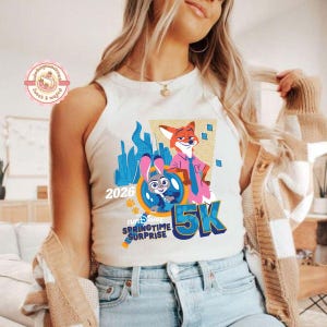 May include: A cream-coloured vest top with a vibrant graphic of cartoon characters, a fox and a bunny, and the text "2026 5K Springtime Surprise". The design includes a cityscape and paw prints.