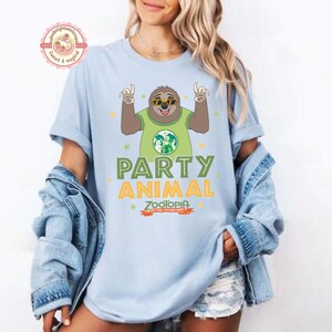 May include: Pale blue t-shirt with a cartoon sloth wearing sunglasses and a green shirt with a world map design. The shirt has the words "PARTY ANIMAL" and "ZOOTOPIA" printed on it in green and orange.