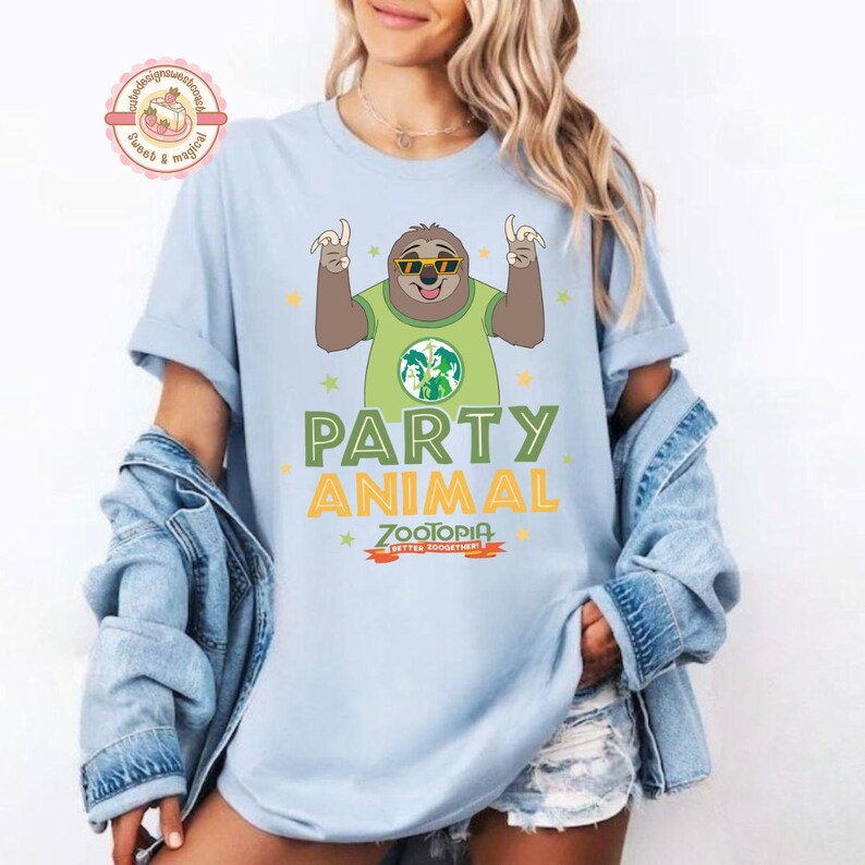 May include: Pale blue t-shirt with a cartoon sloth wearing sunglasses and a green shirt with a world map design. The shirt has the words "PARTY ANIMAL" and "ZOOTOPIA" printed on it in green and orange.