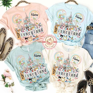 May include: Four pastel-colored t-shirts with a Disneyland graphic. Each shirt features a castle, balloons, and Disney characters. The word "Disneyland" and the year "2020" are printed on the front. The shirts are light pink, light blue, mint green, and cream.