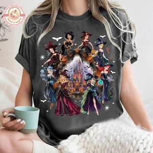 May include: A charcoal gray short-sleeve t-shirt featuring a graphic print of various animated princesses dressed in witch costumes. The design includes a central castle, bats, and stars, arranged in a circular pattern around the characters.