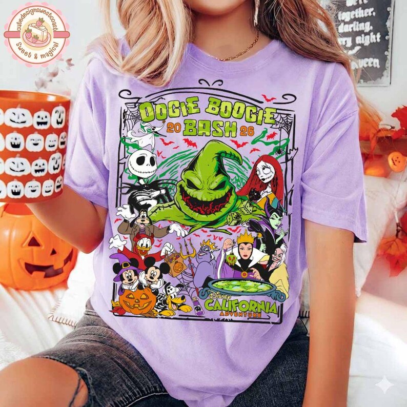 K&ouml;nnte beinhalten: Ein hellviolettes T-Shirt mit einem Grafikdruck des Oogie Boogie Bash 2024 California, der verschiedene Disney-Figuren wie Jack Skellington, Sally, Maleficent und Mickey Mouse in Halloween-Kost&uuml;men zeigt, umgeben von Spinnennetzen und Flederm&auml;usen.