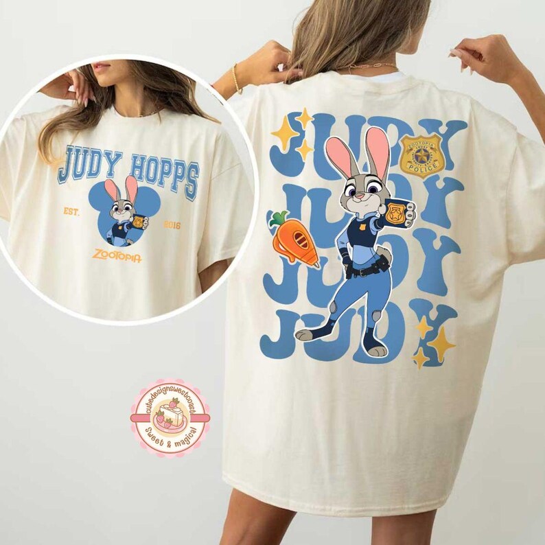 May include: Cream-colored t-shirt featuring a cartoon image of Judy Hopps from Zootopia. The front design includes the text "JUDY HOPPS" and a cartoon image of Judy. The back of the shirt has a larger image of Judy Hopps with the text "JUDY".