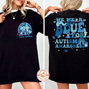 May include: Black t-shirt with a blue graphic on the front featuring cartoon characters and the text "TEAM THOMAS". The back of the shirt has the text "WE WEAR BLUE FOR AUTISM AWARENESS" with additional graphics.