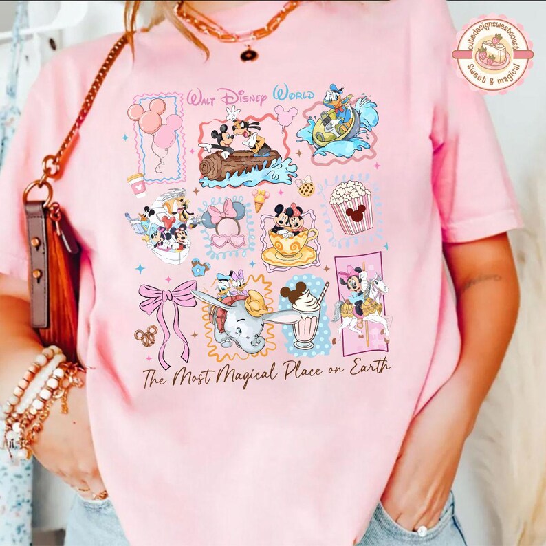 May include: Pink t-shirt featuring a colorful collage of Disney characters and icons. The design includes Mickey and Minnie Mouse, Donald Duck, Dumbo, and popcorn. Text reads "Walt Disney World" and "The Most Magical Place on Earth."