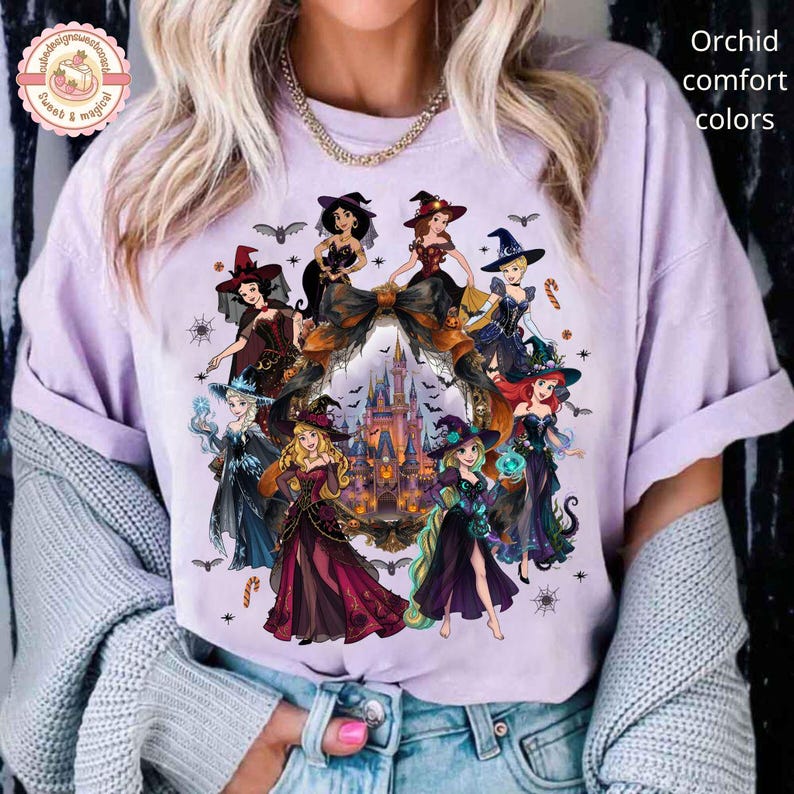 May include: A light purple t-shirt featuring a graphic print of various animated princesses dressed in witch costumes surrounding a central castle illustration. The design includes bats, spiderwebs, and candy canes, with the text Orchid comfort colors.