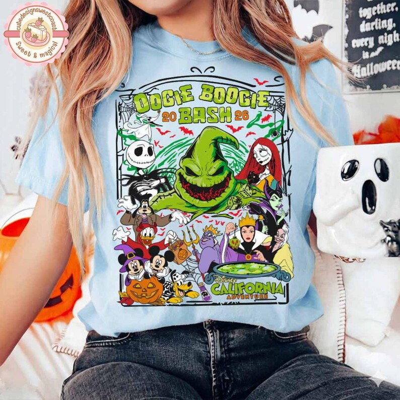 K&ouml;nnte beinhalten: Ein hellblaues T-Shirt mit einem Grafikdruck von Oogie Boogie und verschiedenen Disney-Figuren in einer Halloween-Szene. Der Text lautet Oogie Boogie Bash 2024 California Adventure. Das Design enth&auml;lt K&uuml;rbisse, Spinnennetze und Flederm&auml;use.