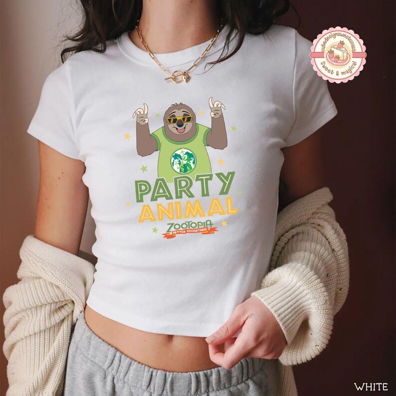 May include: White t-shirt with a cartoon sloth wearing sunglasses and a green shirt with a globe design. The shirt has the words "PARTY ANIMAL" and "Zootopia" printed on it. The t-shirt is a crew neck style.