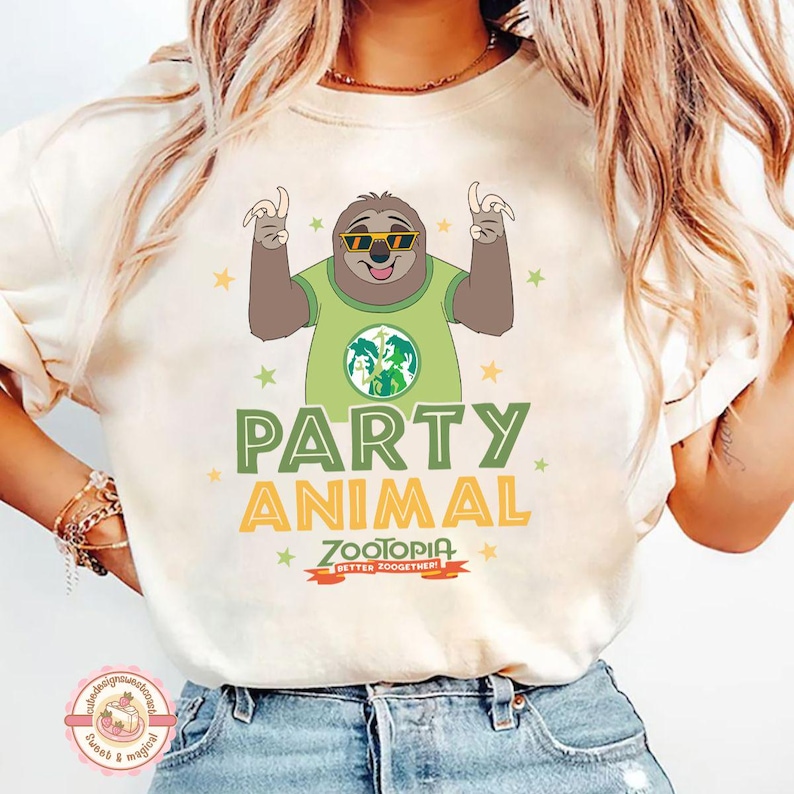 May include: Cream-coloured t-shirt with a cartoon sloth wearing sunglasses and a green shirt with a graphic. The shirt has the words "PARTY ANIMAL" in green and yellow, with "ZOOTOPIA" below. The design includes stars.