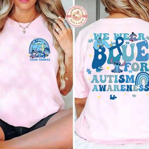 May include: Pale pink t-shirt with a cartoon graphic and the text "TEAM THOMAS" on the front. The back of the shirt has the words "WE WEAR BLUE FOR AUTISM AWARENESS" with cartoon characters and a rainbow design.