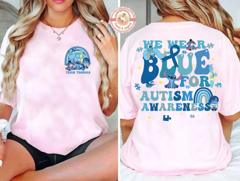 May include: Pale pink t-shirt with a cartoon graphic and the text "TEAM THOMAS" on the front. The back of the shirt has the words "WE WEAR BLUE FOR AUTISM AWARENESS" with cartoon characters and a rainbow design.