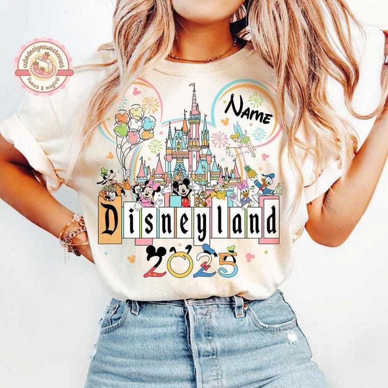 May include: A white t-shirt with a colorful graphic of Mickey Mouse and other Disney characters in front of Cinderella's Castle. The text "Disneyland 2023" is printed below the graphic. The text "Name" is printed above the castle.