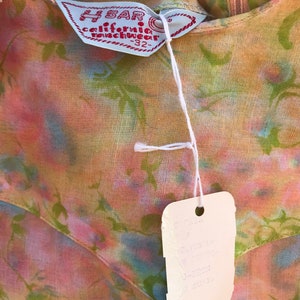 May include: Close-up of a vintage floral dress with a tag. The dress features a colorful pattern of pink, green, and blue hues. The tag reads "H BAR california ranchwear -32" and includes additional text.