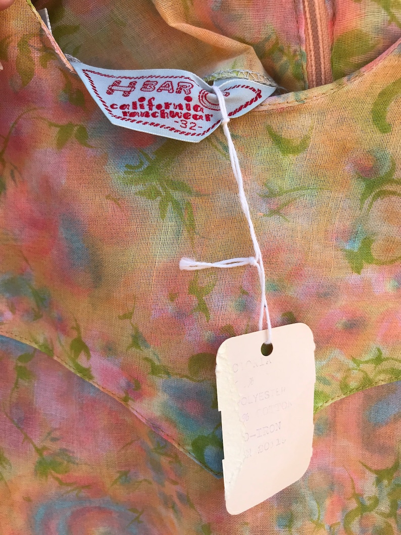 May include: Close-up of a vintage floral dress with a tag. The dress features a colorful pattern of pink, green, and blue hues. The tag reads "H BAR california ranchwear -32" and includes additional text.