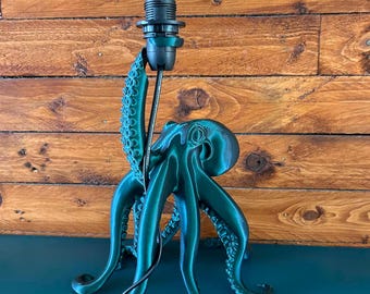 May include: A dark green octopus-shaped lamp base with a black socket and a clear glass Edison-style light bulb. The octopus has textured tentacles with visible suckers, and one tentacle extends upward to support the light fixture and black cord.