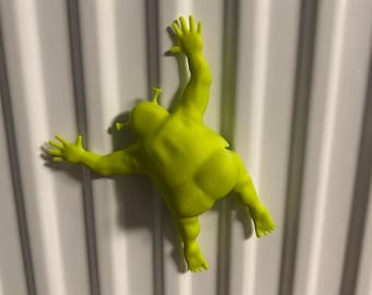 May include: A lime green figurine of a cartoon ogre climbing a white surface. The ogre has outstretched arms and legs, with detailed hands and feet. The figurine is a vibrant, solid color and appears to be made of plastic or a similar material.