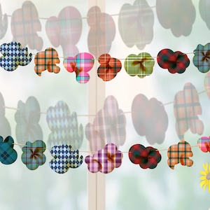 May include: A decorative garland of fabric cloud and flower shapes in various plaid patterns, strung across a window. The clouds are in shades of purple, blue, orange, and green. A yellow star and wooden house are on the windowsill.