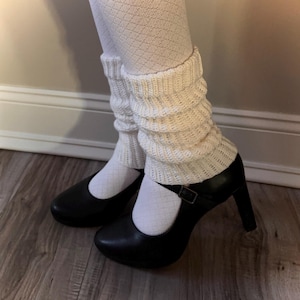 Puede incluir: Zapatos de tacón negros estilo Mary Jane con cierre de hebilla combinados con medias blancas con estampado de rombos y calentadores de piernas color crema. Los calentadores son de punto y están arrugados alrededor de los tobillos.