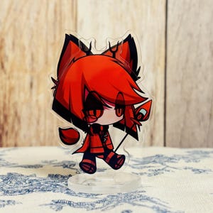 Op de afbeelding: Een rood en zwart anime-figuur met hoorns en een staart. Het figuur houdt een rood en zwart staf vast. Het figuur staat op een doorzichtige plastic basis.