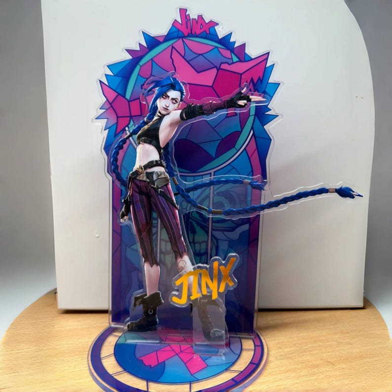 May include: A colorful acrylic stand featuring Jinx, a character from the video game League of Legends. The stand has a stained glass design with a blue, pink, and purple color scheme. Jinx is depicted with her signature blue hair and a purple and black outfit. The stand is a great way to show off your love for the game.
