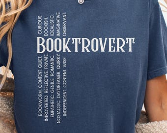 May include: A navy blue t-shirt with the word "BOOKTROVERT" in large white letters. The shirt also features a list of words describing personality traits, such as "curious" and "bookish."